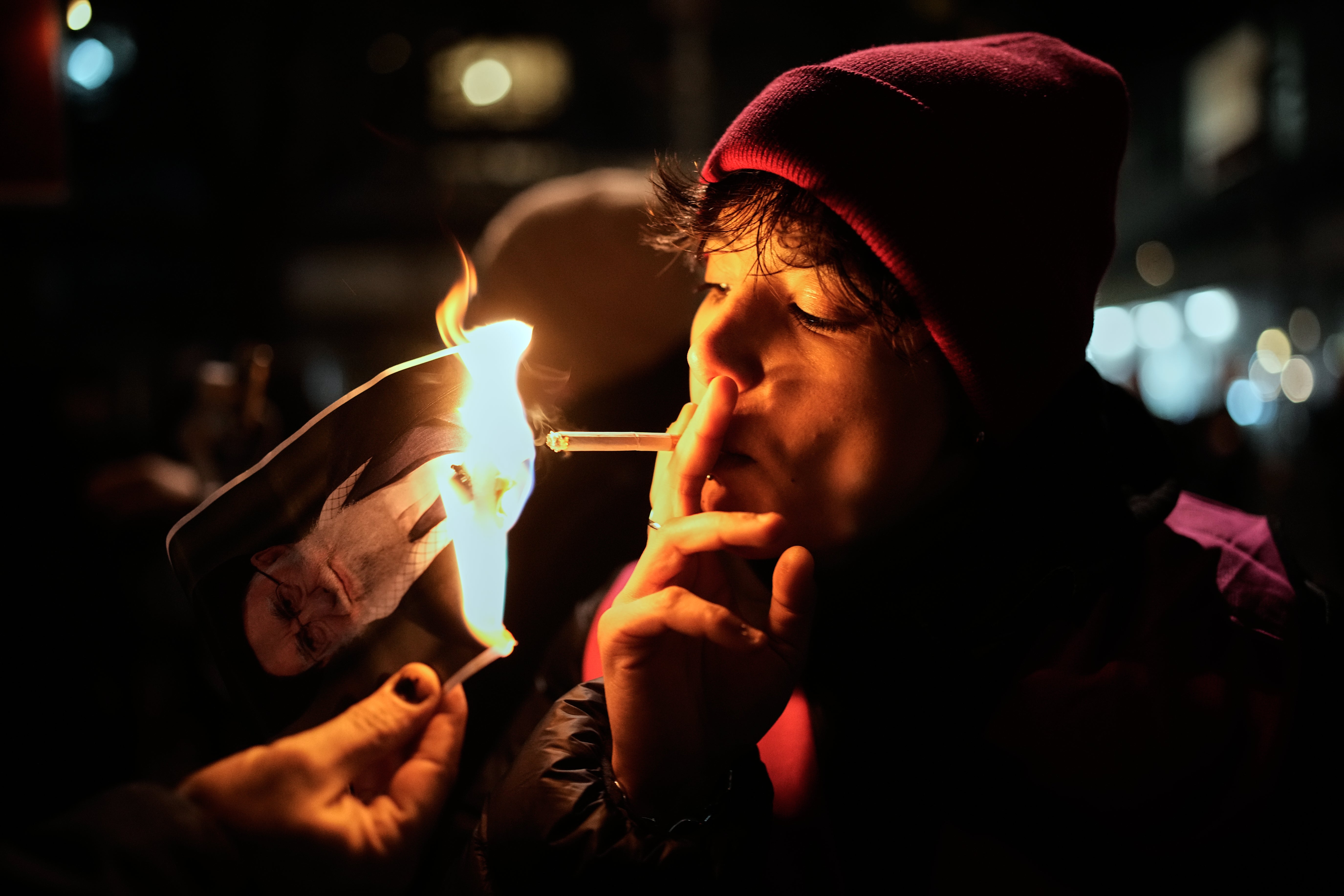 A protester lights a cigarette over a burning poster of Iran's Supreme Leader Ayatollah Ali Khamenei during a demonstration in Berlin, Germany, Wednesday, January 14, 2026, in support of massive nationwide protests against the government. (AP Photo/Ebrahim Noroozi)
