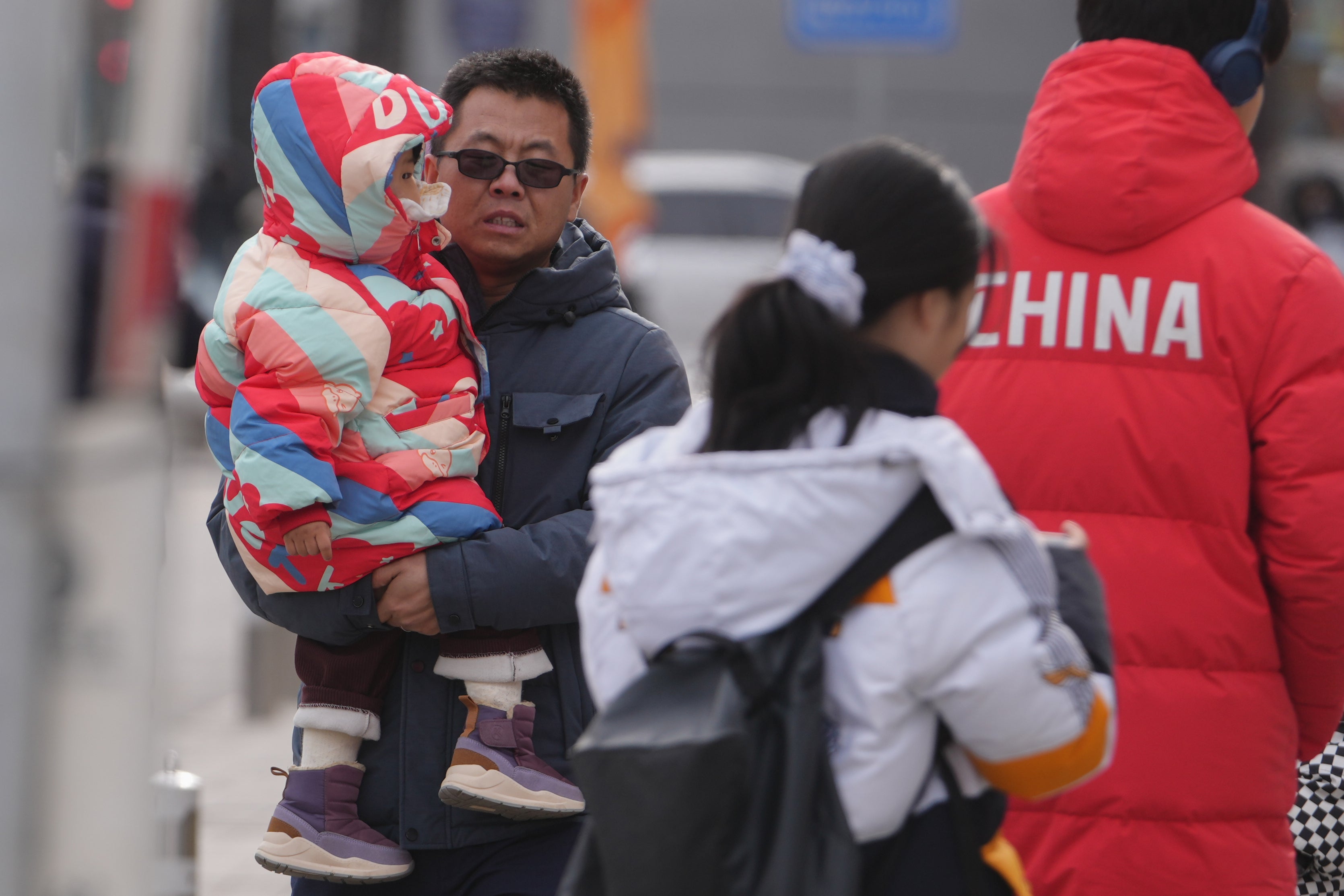 On Monday, January 19, 2026, a man walked on the streets of Beijing holding a young child in his arms. (AP Photo/Andy Wong)