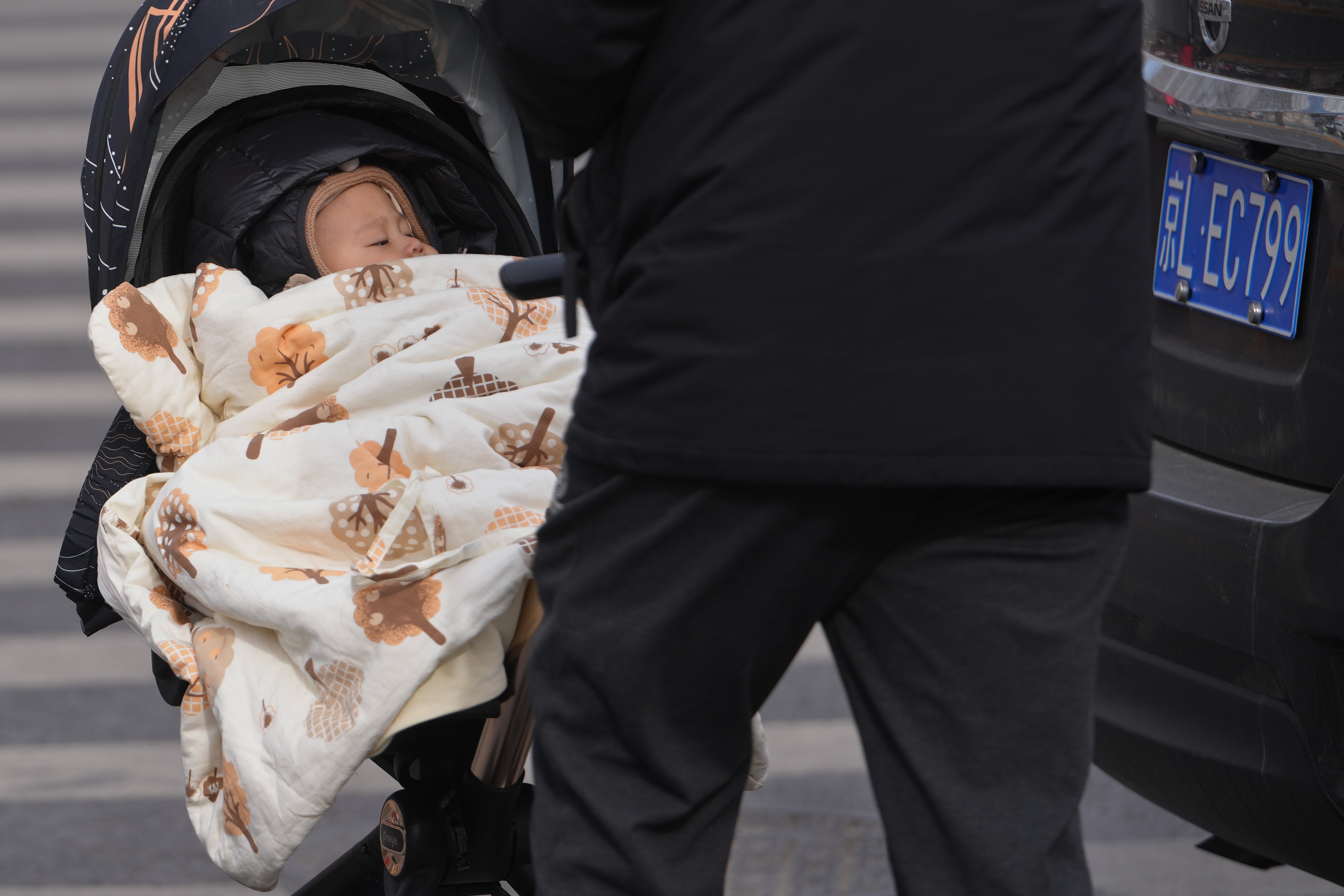 On Monday, January 19, 2026, a man pushed a toddler in a stroller on the streets of Beijing. (AP Photo/Andy Wong)