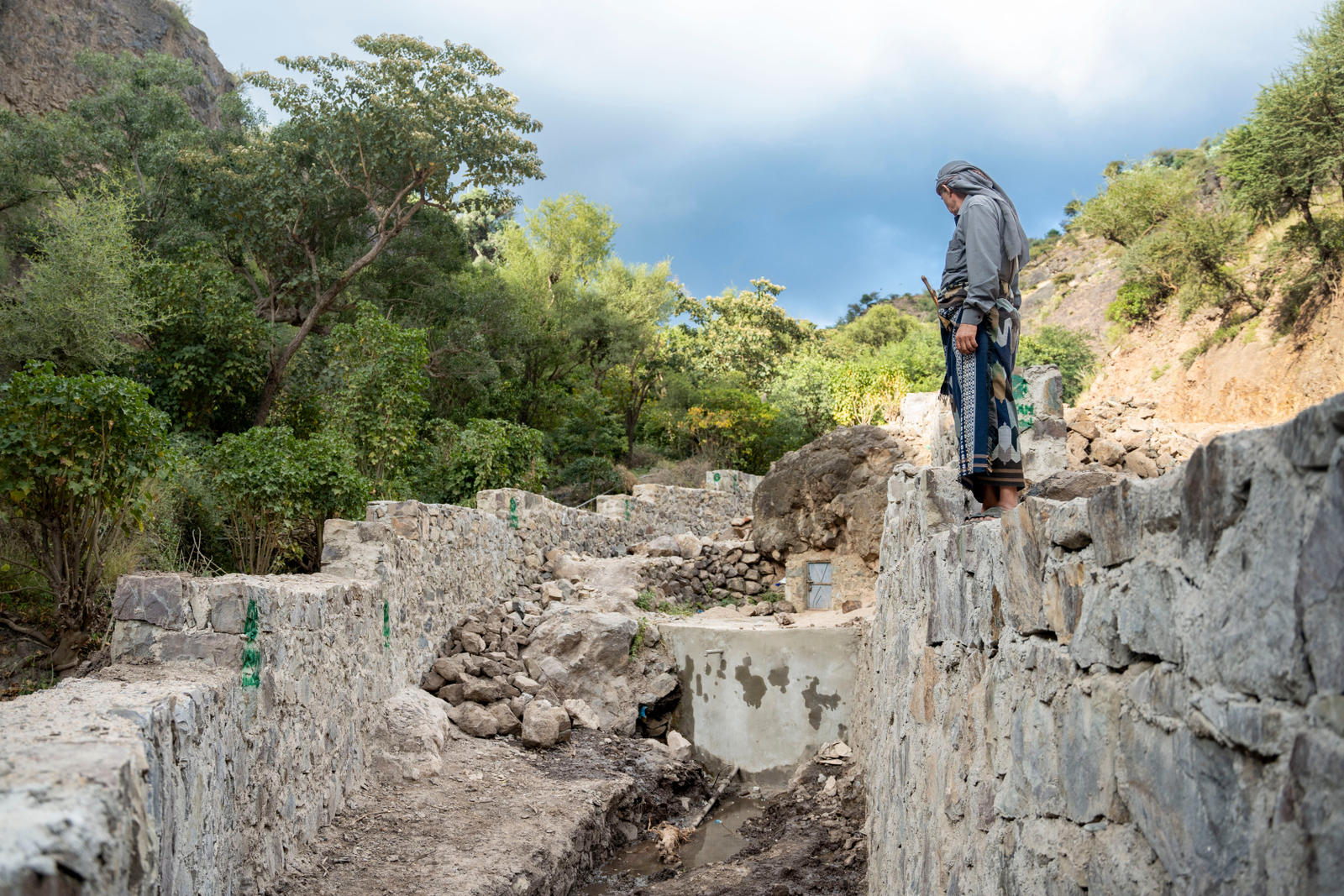 Jameel Mahyoub Saif, 55, poses next to his village's water infrastructure, which has been repaired with concrete