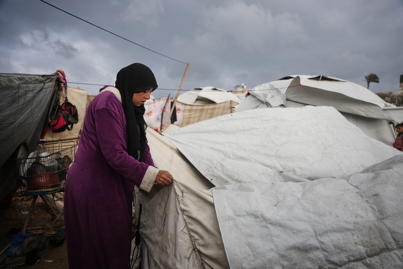 In a displacement camp in Zawaida, Yasmin Shalha mends her torn tent that was damaged by a storm.