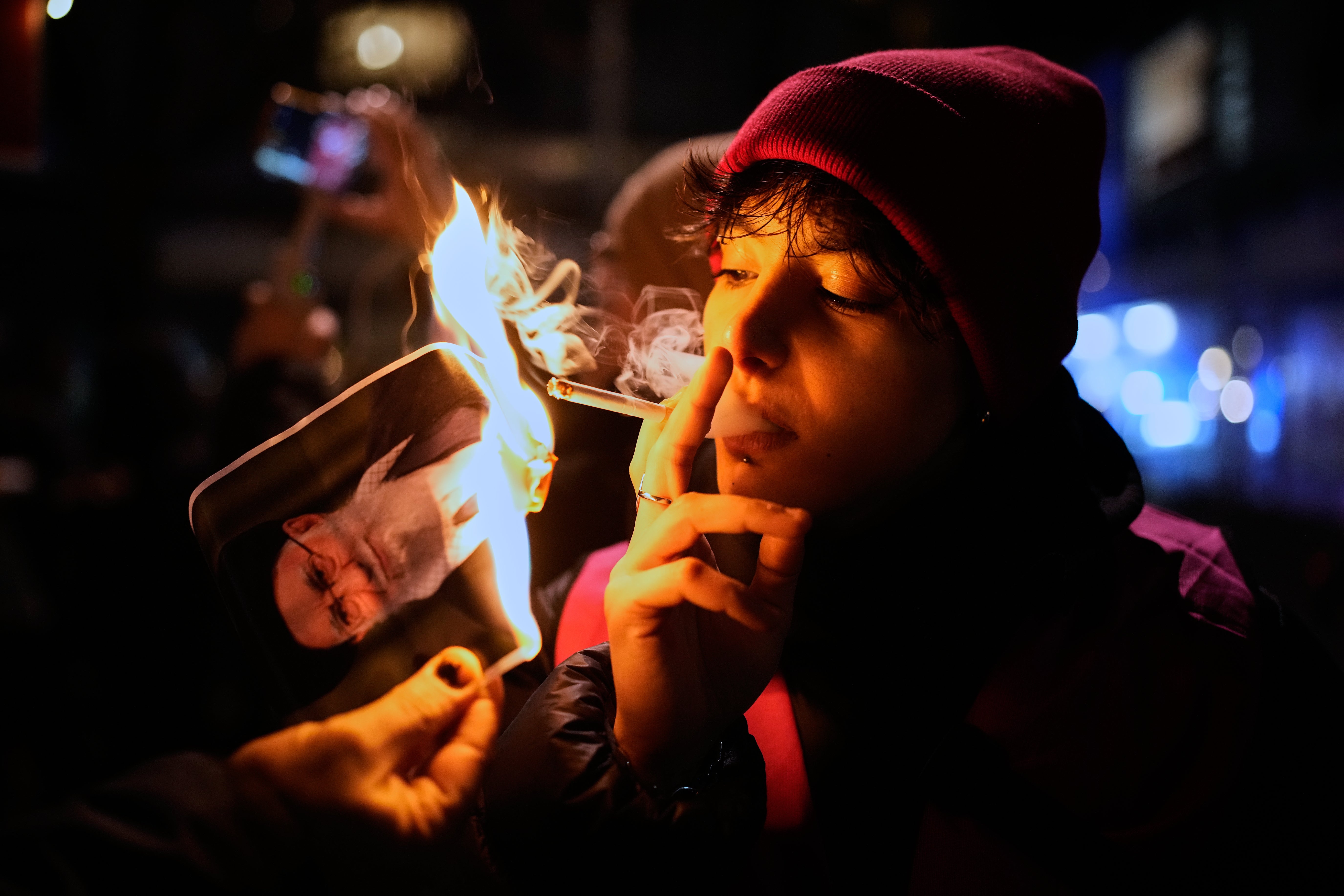 A protester smokes a cigarette after setting fire to a poster of Iran's Supreme Leader Ayatollah Ali Khamenei during a demonstration in support of massive nationwide protests against the government in Iran in Berlin, Germany, Wednesday, January 14, 2026